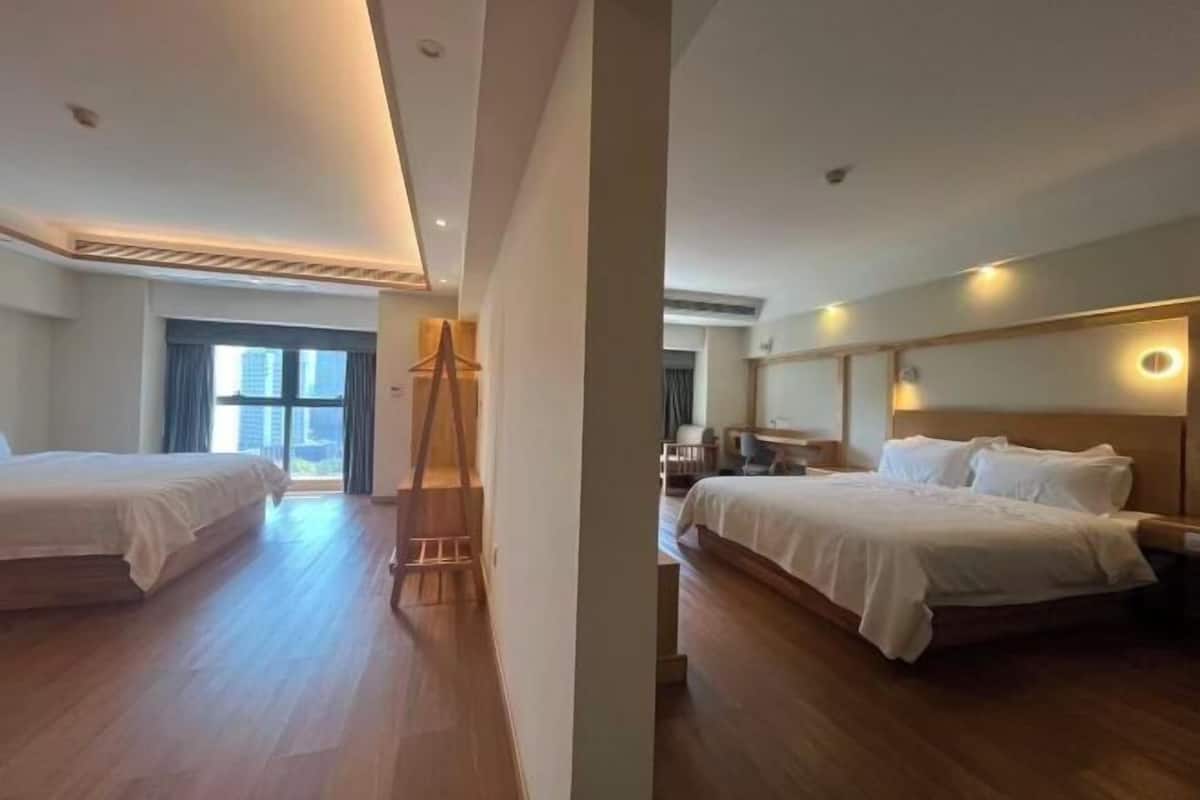 A hotel room with two beds, a wooden floor, a large window, and a desk with a chair.