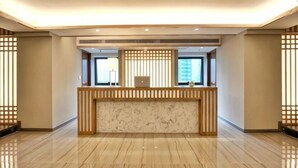 Zona de recepción de hotel con mostrador de mármol, ventanas amplias y diseño de interiores moderno.