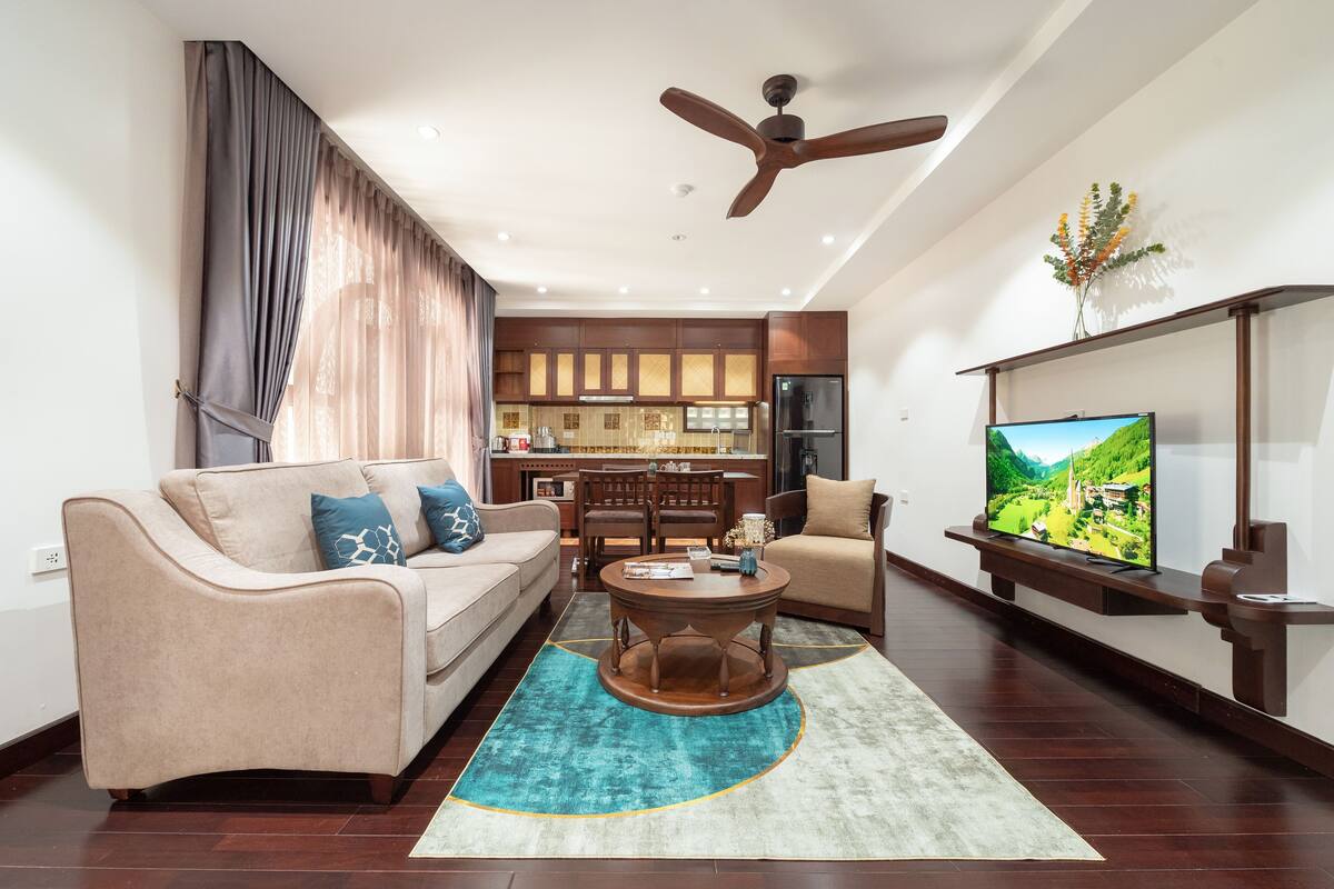 A modern living room with a sofa, coffee table, and TV. A kitchen is visible in the background.