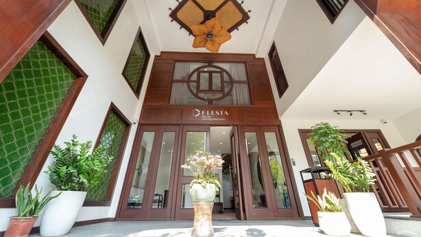A hotel entrance with a large flower decoration, a sign reading "FLESTA," and potted plants. - Flesta Doi Can (Hanoi)