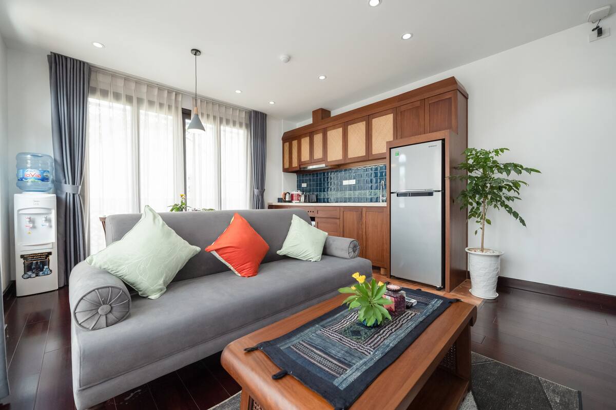 A modern living room with a grey sofa, wooden cabinets, a water dispenser, and a potted plant.