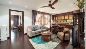 A modern living room with a sofa, coffee table, and TV. There is a kitchen area with cabinets and a refrigerator. - Flesta Doi Can (Hanoi)