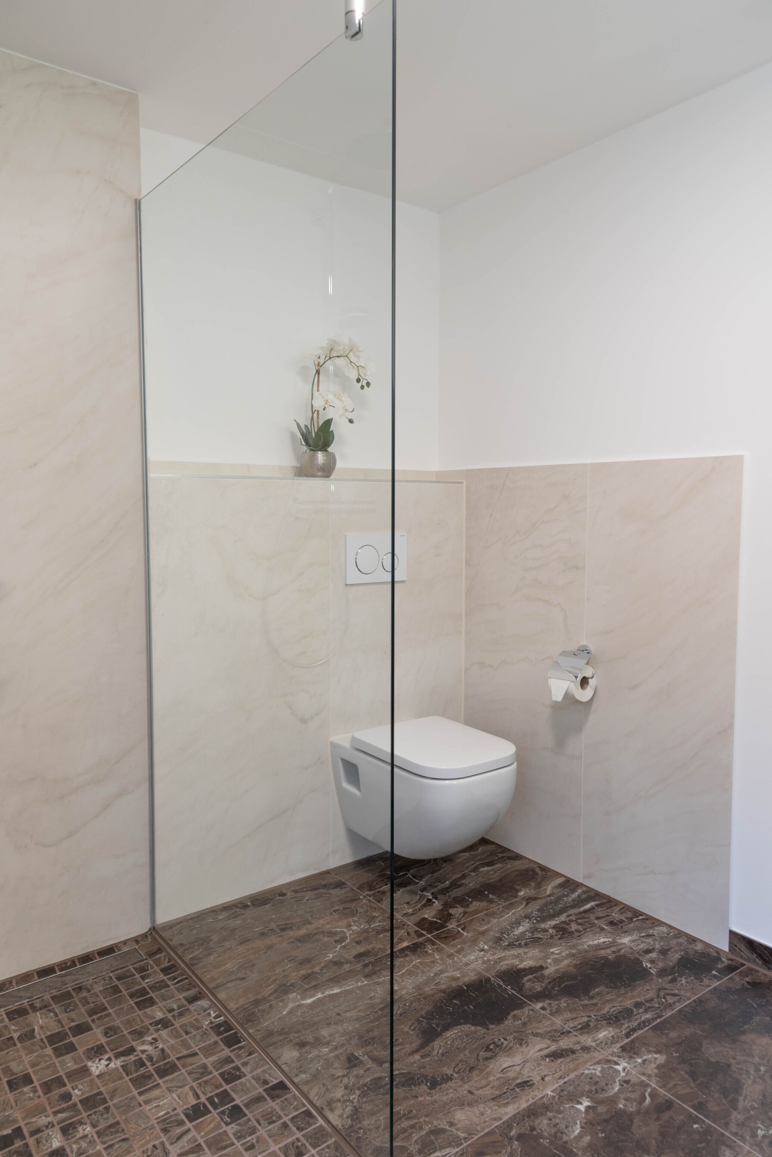 Un baño moderno con cabina de ducha de vidrio, inodoro y suelo de mármol.