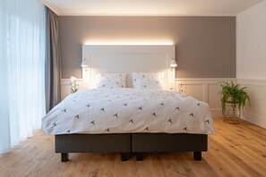 A double bed with a patterned bedspread, bedside lamps, a potted plant, and a wooden floor. - OSCARS Hotel 1415 (Bad Liebenzell)