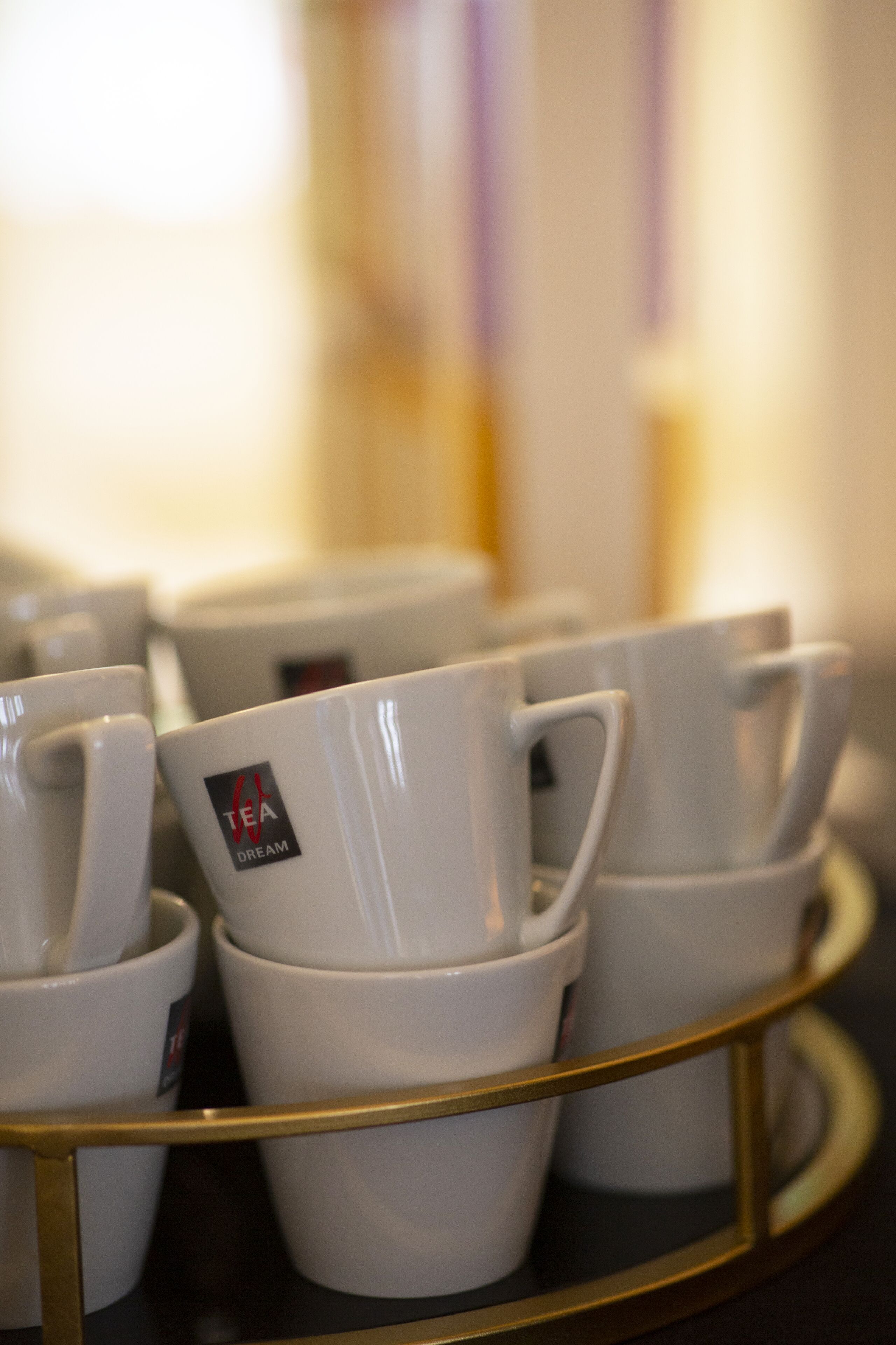 A tray with several white cups, some with a tea logo, on a gold-colored tray.