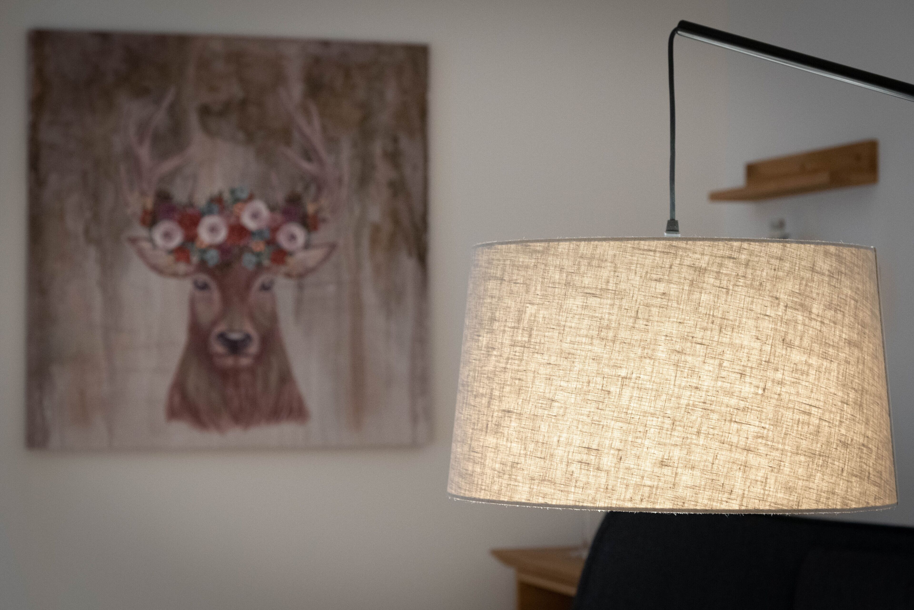 A lamp with a textured shade and a painting of a deer on the wall.