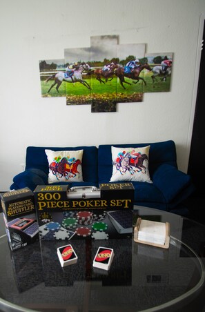 Uma sala de estar com um sofá azul, duas almofadas com tema de cavalos e uma mesa de centro de vidro exibindo fichas de pôquer e um conjunto de cartas.