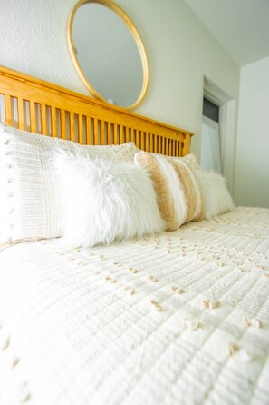 Een bed met een witte sprei en zachte kussens, een houten hoofdbord en een ronde spiegel erboven.