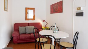 A red sofa with cushions, a small round table with chairs, a red lamp, and a wall-mounted mirror. - Opera House - Monti Area (Rome)
