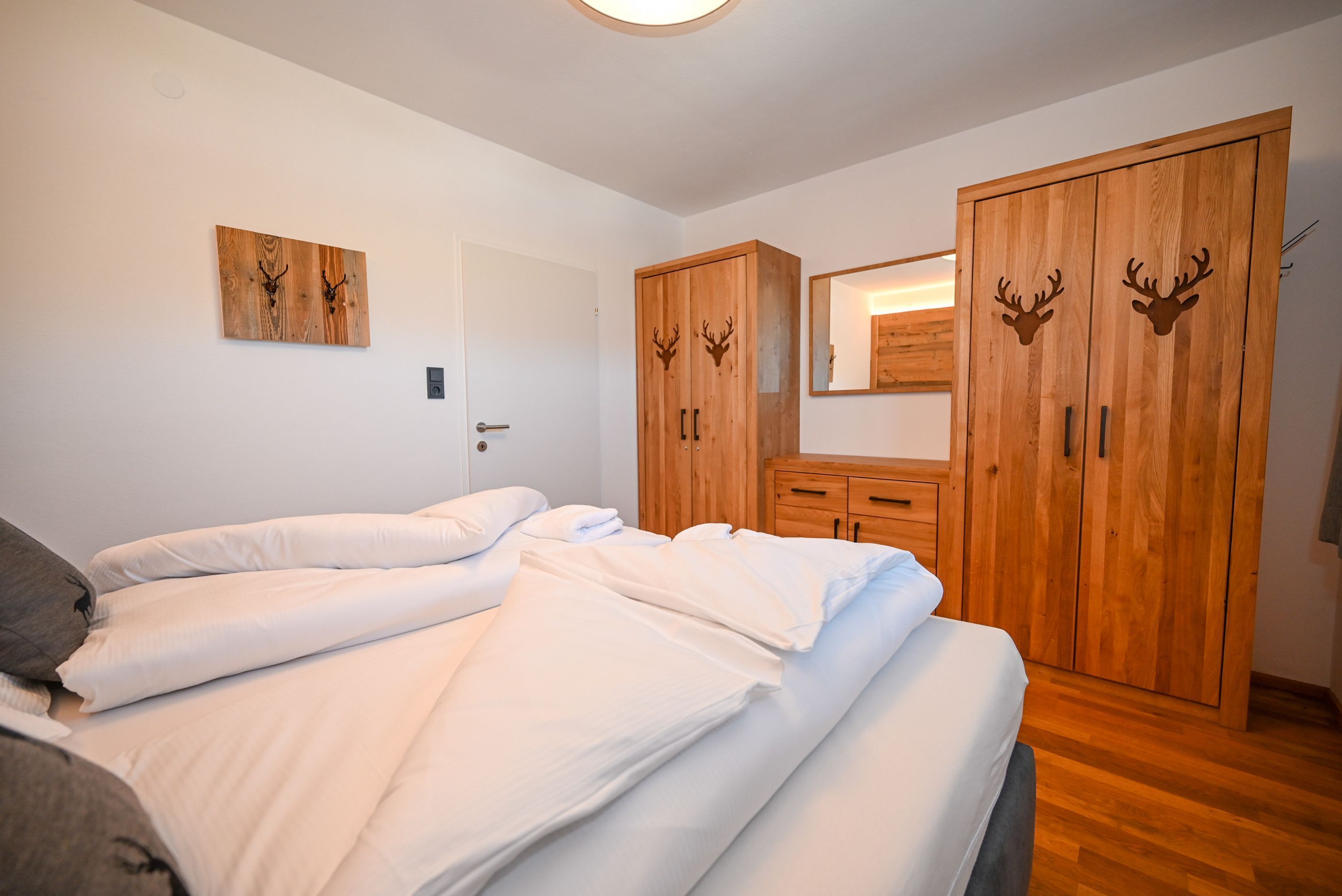 Ein Schlafzimmer mit zwei Betten, Holzschränken mit Hirschgeweih-Schnitzereien und einem an der Wand befestigten Spiegel.