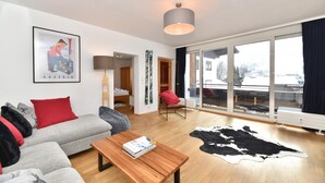 A modern living room with a sofa, a coffee table, and a large window offering a view of a snowy landscape. - Domizil Thirteen - Sauna and Glacier View (Kaprun)