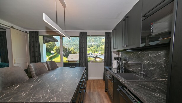 A modern kitchen with a marble countertop, a built-in oven, and a view of a green landscape. - Domizil Thirteen - Sauna and Glacier View (Kaprun)
