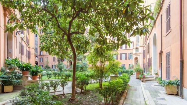 A courtyard with potted plants and a tree, surrounded by buildings with arched windows and balconies. - La Casa dell'Arte by Interhome (Rome: Historical City Center)