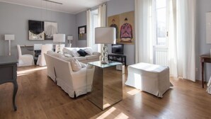A modern living room with a sofa, a coffee table, and a TV. There is a window with curtains, a painting on the wall, and a lamp. - La Casa dell'Arte by Interhome (Rome: Historical City Center)