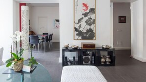 Una sala de estar moderna con una mesa de centro de vidrio, orquídeas blancas, una consola negra con objetos decorativos y un cuadro grande en blanco y negro en la pared.