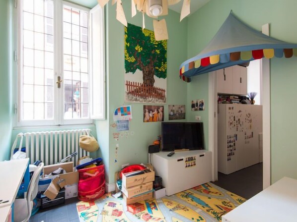 A child's playroom with a large window, a tree mural, a play tent, and a TV.