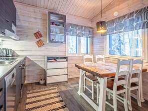 Una cocina moderna con armarios de madera, horno integrado y comedor con sillas blancas y mesa de madera.