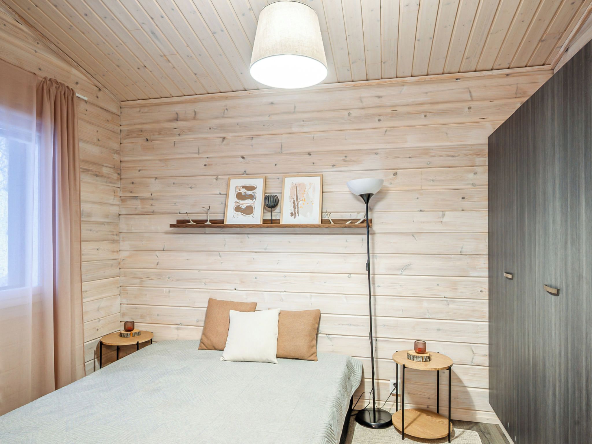 A bedroom with a bed, a bedside table, a floor lamp, and a shelf with artwork.