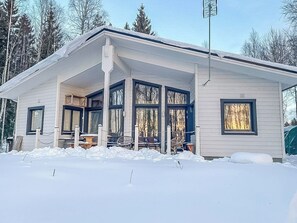 Une maison de plain-pied avec un porche abrité, de grandes fenêtres et un paysage enneigé.