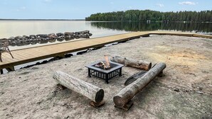 A lakeside deck with a fire pit, logs, and a chair.