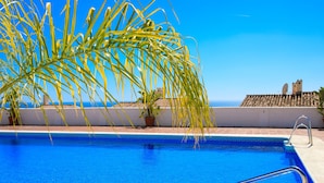 En klar blå pool med metalgelændere, omgivet af plantekasser og udsigt til havet.