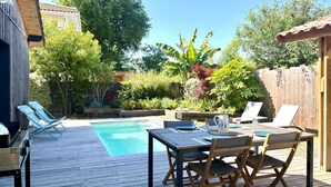 Une terrasse en bois avec une piscine, du mobilier d’extérieur et une végétation luxuriante.