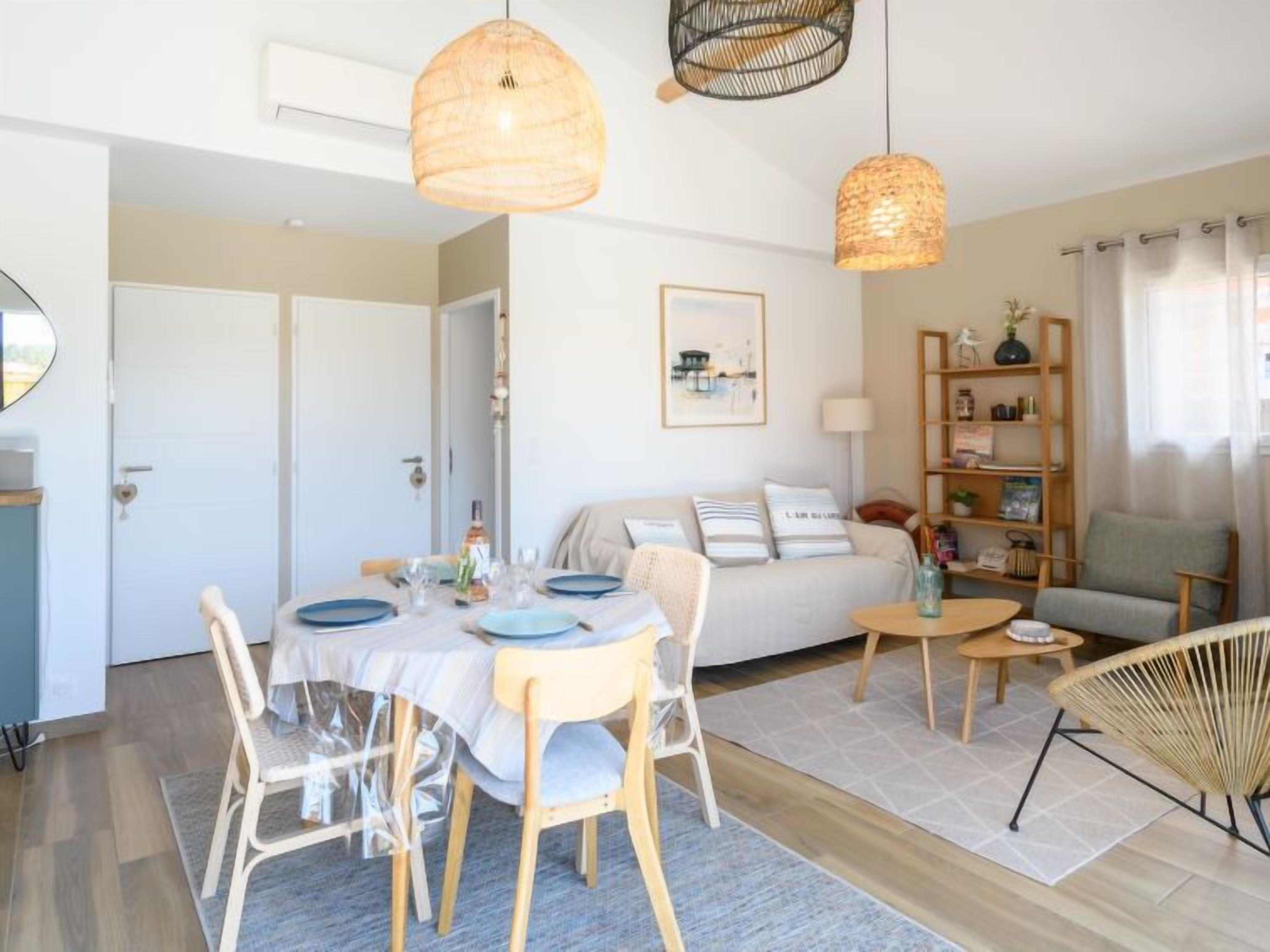 A modern living room with a dining area, featuring a sofa, a coffee table, a bookshelf, and a dining table set with plates and glasses.