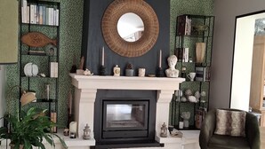 Een woonkamer met een open haard, een ronde spiegel en een boekenkast.