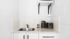 A kitchen with a stainless steel sink, white cabinets, a microwave, and a coffee maker on the countertop. - Beach Views on Excellent Studio 27 - Belle Escapes Jervis Bay (Vincentia)