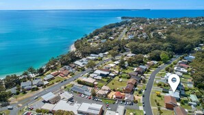 An aerial view of a coastal residential area with houses, roads, and a beach. - Beach Views on Excellent Studio 27 - Belle Escapes Jervis Bay (Vincentia)