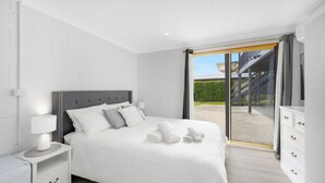 A modern bedroom with a large bed, a nightstand, a dresser, and a sliding glass door leading to a balcony. - Beach Views on Excellent Studio 27 - Belle Escapes Jervis Bay (Vincentia)