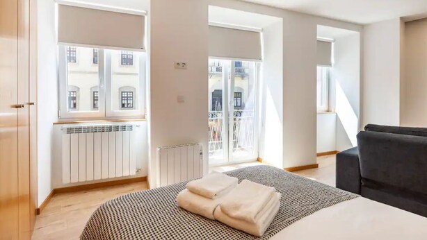 Un dormitorio moderno con una cama grande, una colcha de diseño blanco y negro, un sofá negro y vistas a un edificio a través de una ventana.