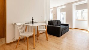 Un salón moderno con una mesa blanca y dos sillas, un sofá negro y un radiador.
