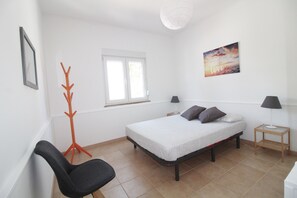 Quarto com cama, poltrona, luminária de chão, mesa de cabeceira e janela.