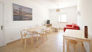 Uma sala de estar moderna com área de jantar, um sofá vermelho, uma televisão e um quadro grande de uma ponte.