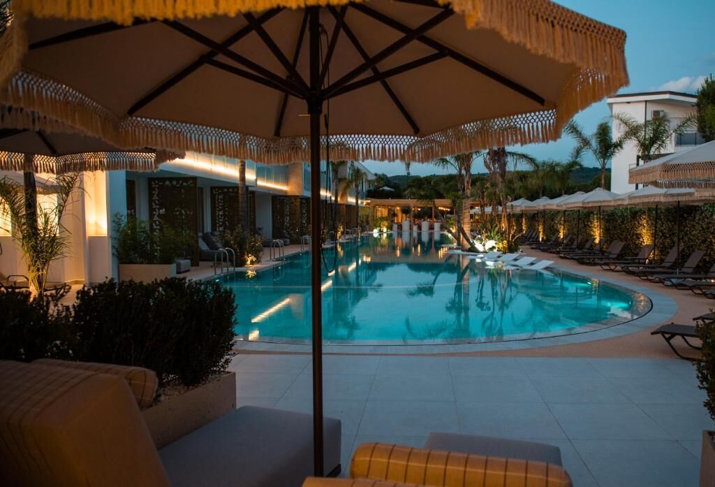 Área de piscina com espreguiçadeiras e guarda-sóis, rodeada por vegetação e arquitetura moderna.
