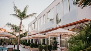 A modern hotel with a pool area, outdoor seating, and palm trees.