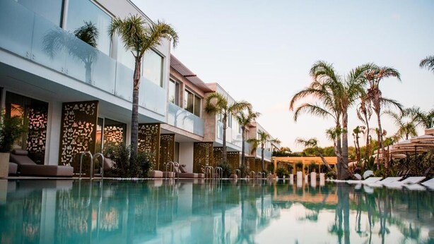 A modern hotel with a pool, palm trees, and lounge areas.