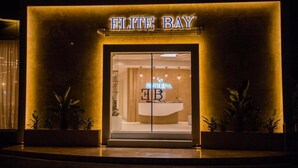 The exterior of a hotel named "ELITE BAY" with a modern design, featuring a prominent entrance and illuminated signage.