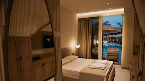 A modern hotel room with a large bed, a wardrobe, and a view of an outdoor pool area.