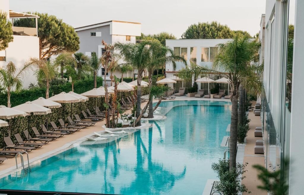A swimming pool with lounge chairs and umbrellas, surrounded by greenery and modern buildings.