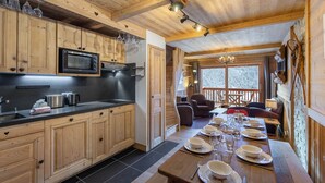 A wooden cabin with a kitchen featuring a microwave, a dining area with a long table set for six, and a cozy seating area with chairs and a fireplace. - Bright duplex for 8 people, near center, Méribel (Méribel)