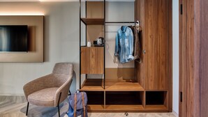 A modern room with a wooden wardrobe, a cushioned chair, and a flat-screen TV mounted on the wall. - Stadthotel Neumarkt Mitte (Neumarkt in der Oberpfalz)