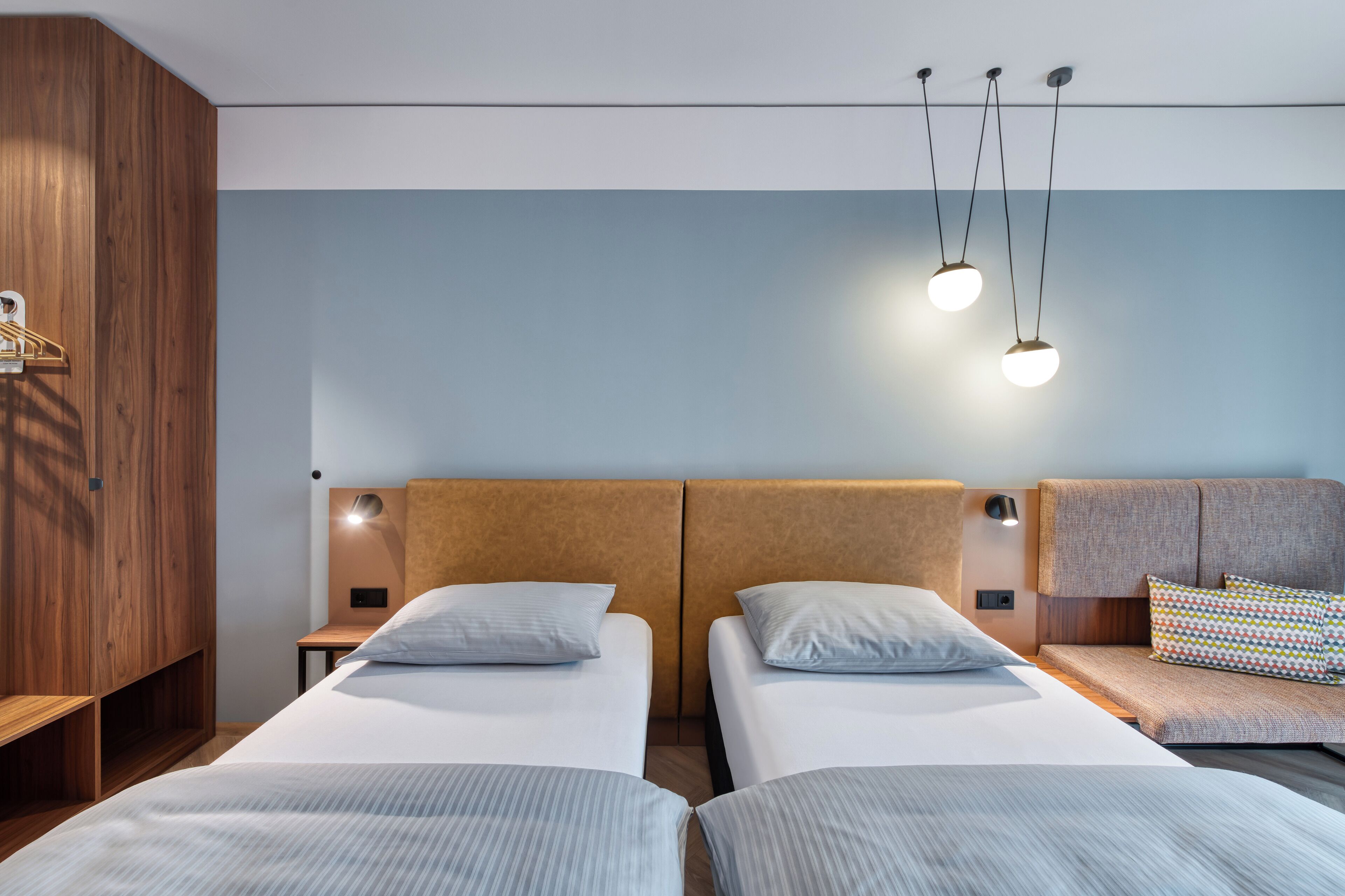 Habitación de hotel con dos camas, un armario de madera y cabecera con iluminación integrada.