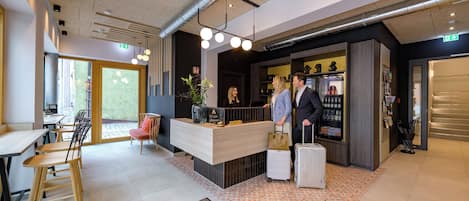 A modern hotel lobby with a reception desk, seating area, and a bar.