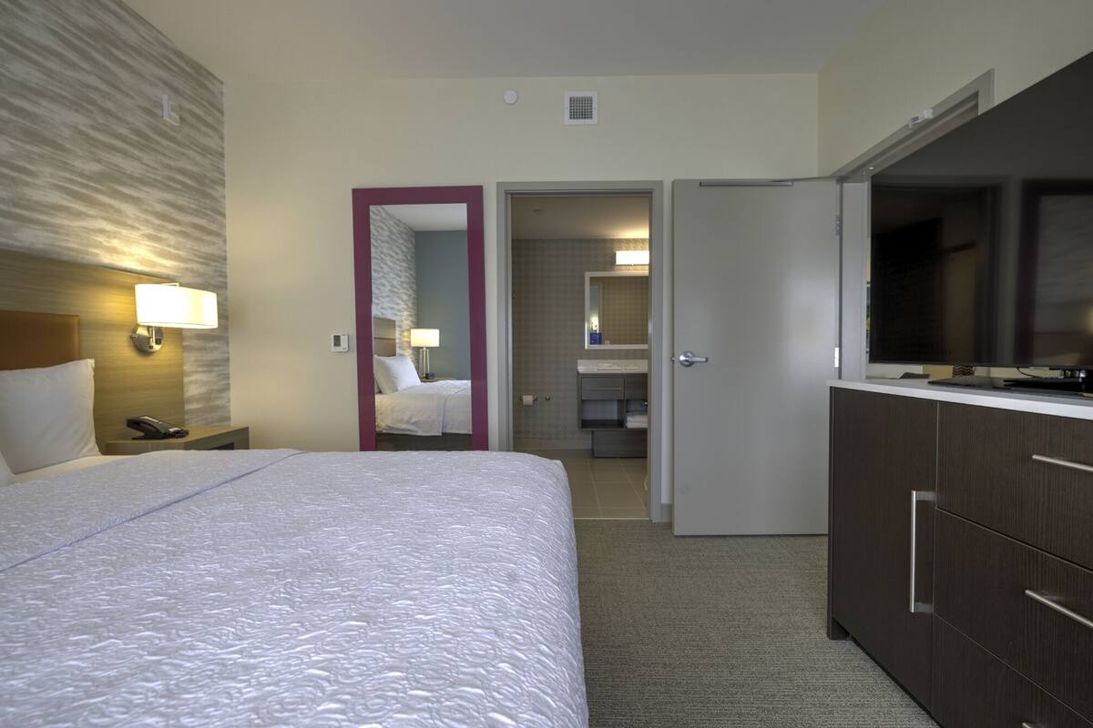 Une chambre d’hôtel avec un grand lit, une télévision, un bureau avec une lampe et une salle de bain visible à travers une porte ouverte.