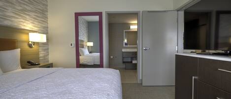 A hotel room with a large bed, a TV, a desk with a lamp, and a bathroom visible through an open door.