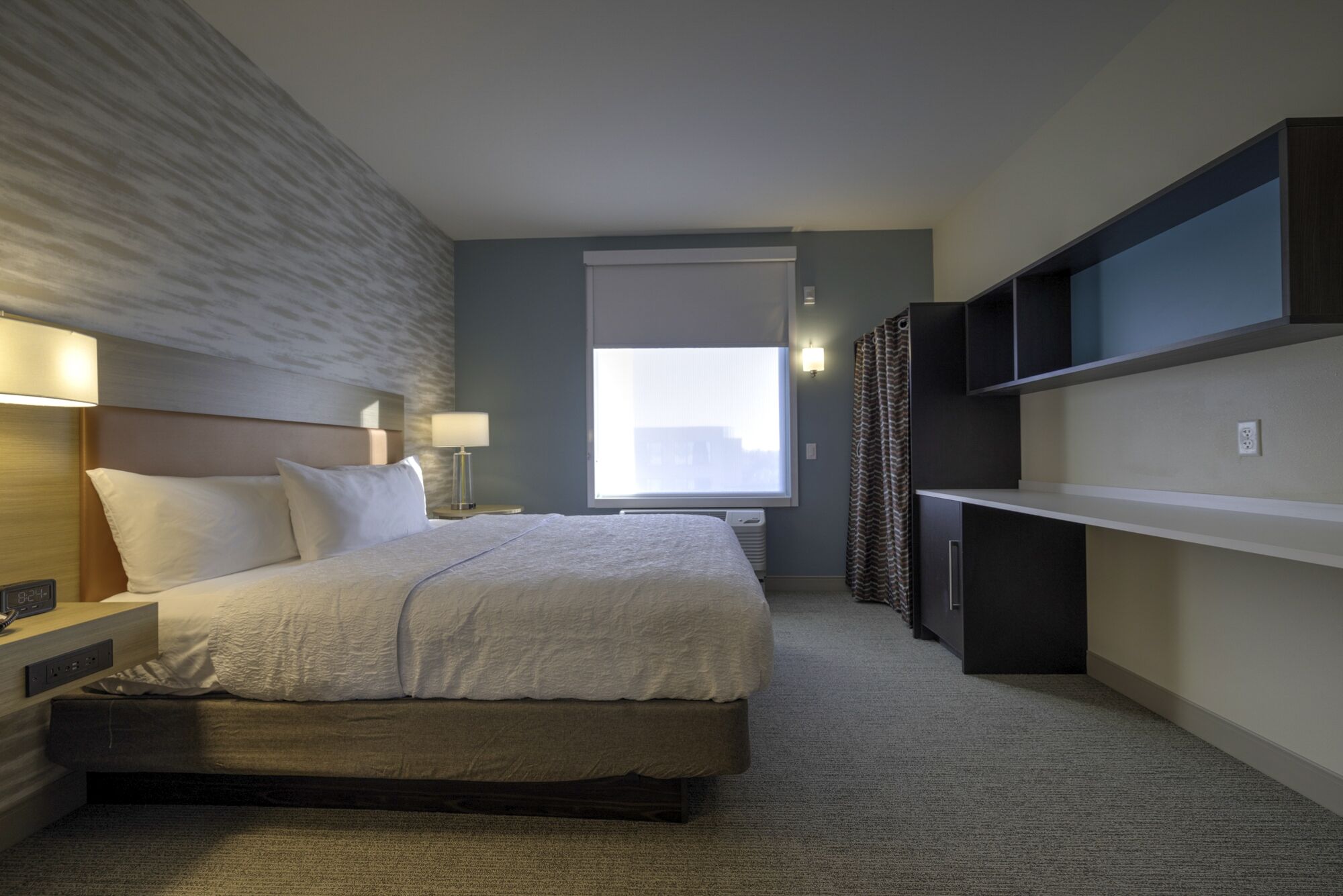 A modern hotel room with a large bed, bedside tables, a desk, and a window with a city view.