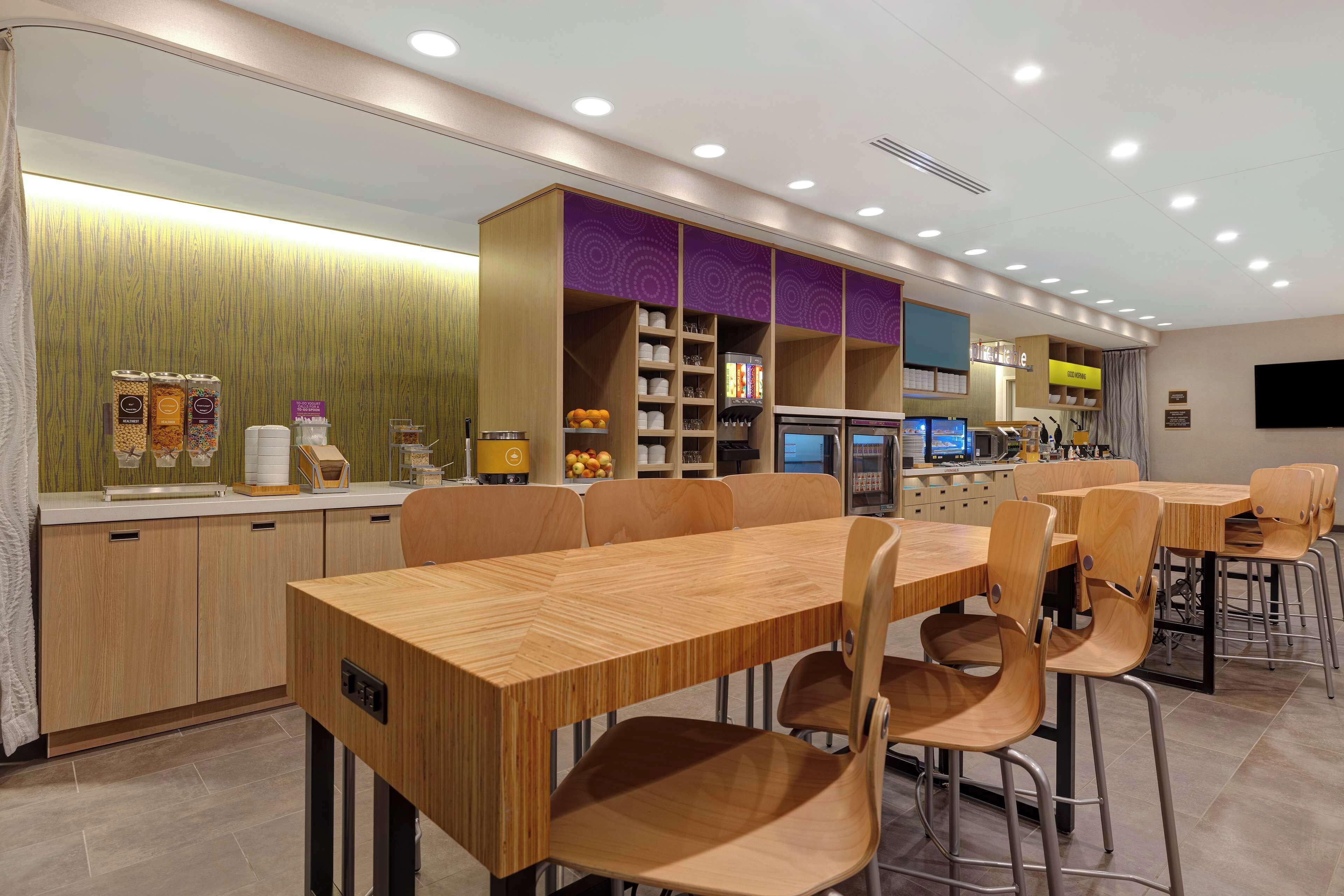 Un restaurant modern amb mobles de fusta, una barra amb begudes i una zona de seients amb taules i cadires.