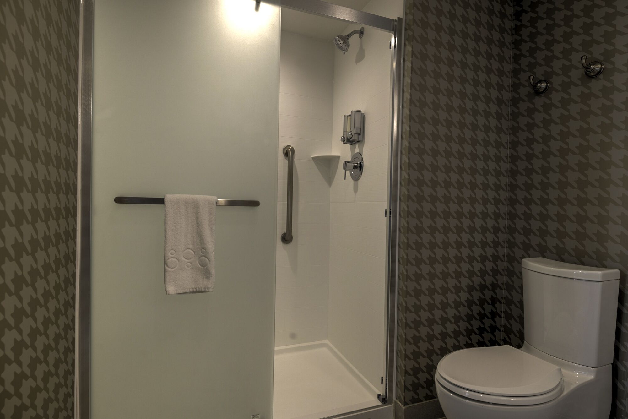 A bathroom with a glass-enclosed shower, a towel rack, a toilet, and patterned wallpaper.